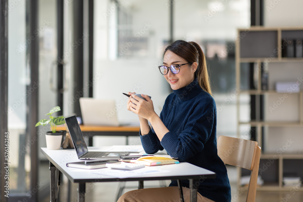 Young Asian professional business woman office worker analyst sitting at desk working on laptop thinking on project plan, analyzing marketing or financial data online, watching elearning webinar.