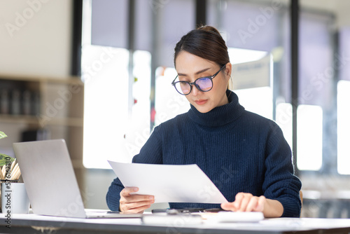 Young Asian professional business woman office worker analyst sitting at desk working on laptop thinking on project plan, analyzing marketing or financial data online, watching elearning webinar. photo