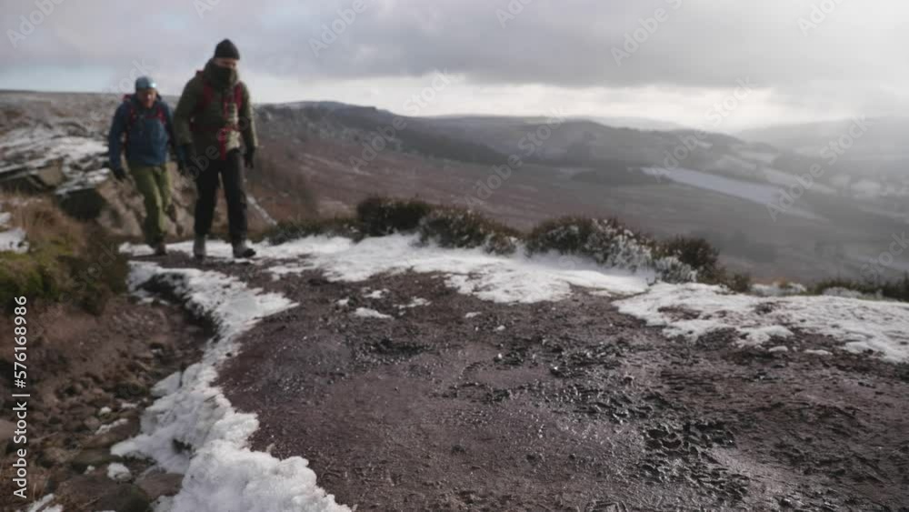 Two people hiking up a muddy, snowy winter path in the rural countryside with an epic view behind them. Two people hiking up a muddy, snowy winter path in the rural countryside with an epic view behind them.
