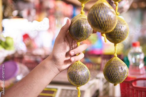 unrecognizable man's hand in close-up holding borojo hanging on netting in marketplace