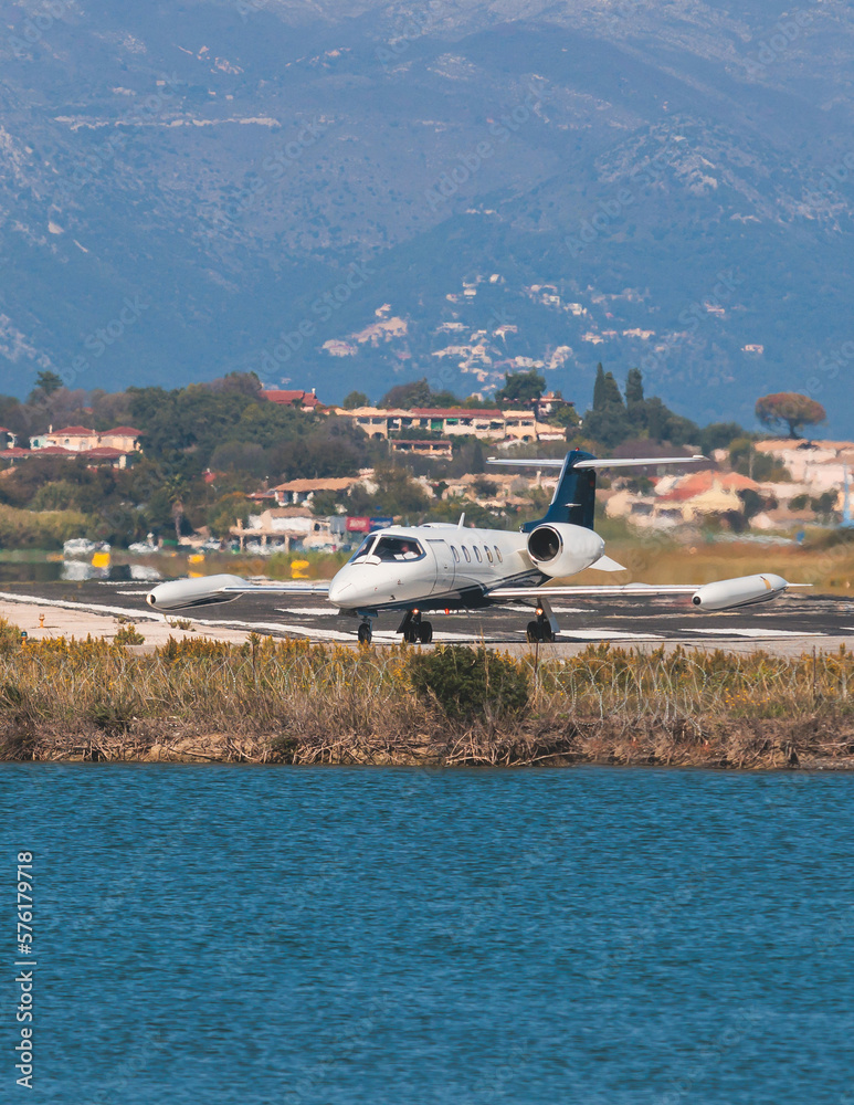 View of modern private reactive aircraft on an runway airfield ready to take off, airstrip with business jet airplane before the flight with mountains in the background in a summer sunny day View of modern private reactive aircraft on an runway airfield ready to take off, airstrip with business jet airplane before the flight with mountains in the background in a summer sunny day