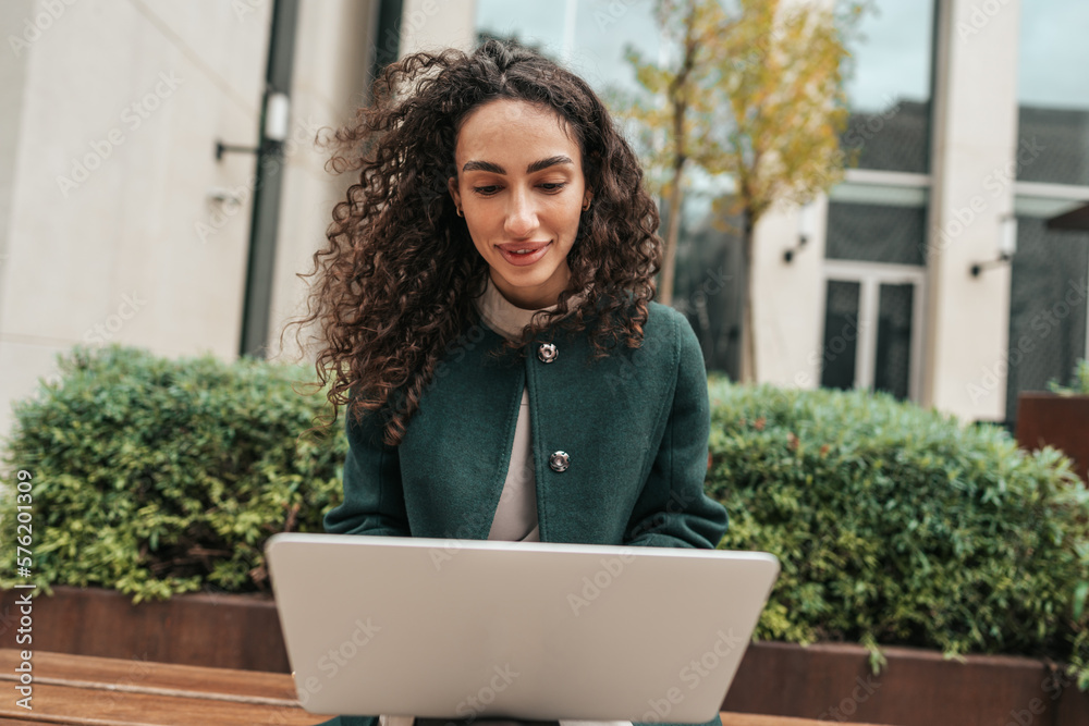 Young woman using laptop while sitting by the building outdoors. Young woman using laptop while sitting by the building outdoors.