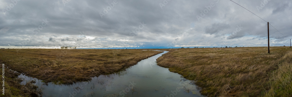 Panorama of a creek meandering through a grass field in winter 