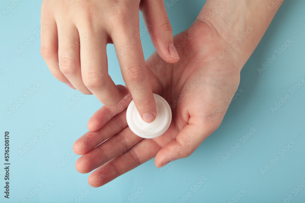 Close up woman hands holding bottle of white face cream touching it with finger on blue background. Skin care Close up woman hands holding bottle of white face cream touching it with finger on blue background. Skin care