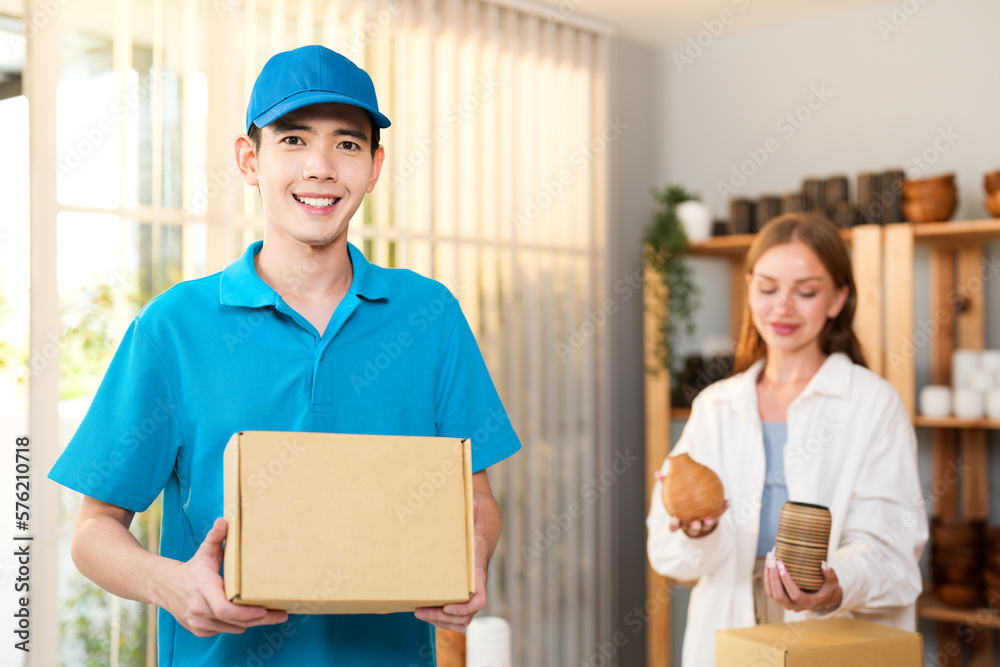 Asian delivery man holding box mockup while Caucasian woman packing vase product for send to customer that online order Asian delivery man holding box mockup while Caucasian woman packing vase product for send to customer that online order