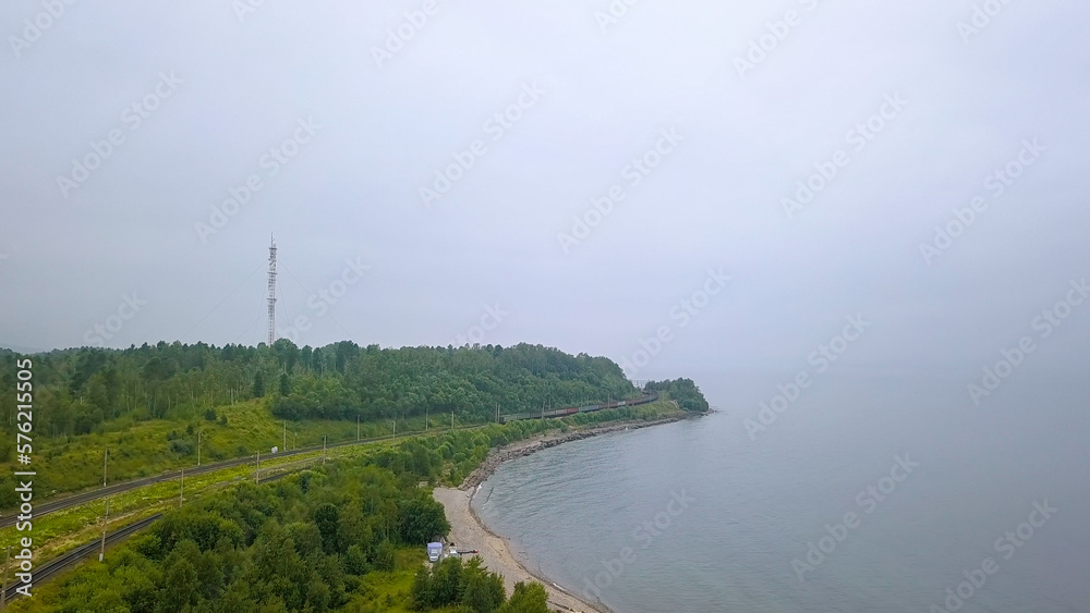 Russia, Baikal - August 02, 2018: Trans-Siberian Railway, coast of Lake Baikal. Train movement along the lake shore, From Drone