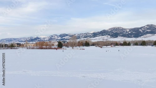 Boseman Montana winter aerial over snowy suburban park with frozen pond, ice fishermen and ice skaters with mountain backdrop during golden hour photo