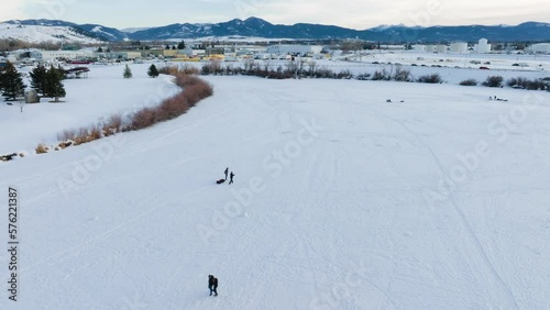 Boseman Montana Winter Aeria over sledders and ice fishermen in snowy suburban park, orbit right with 4k drone over with mountain backdrop at sunset photo