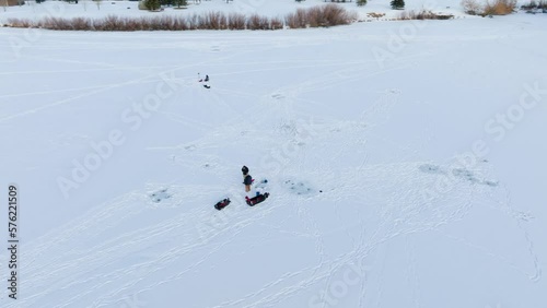 Boseman Montana ice fishermen on snowy frozen suburban pond, tracking right with 4k drone during golden hour photo