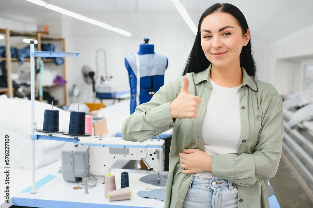 Fototapeta premium Young woman working as seamstress in clothing factory.