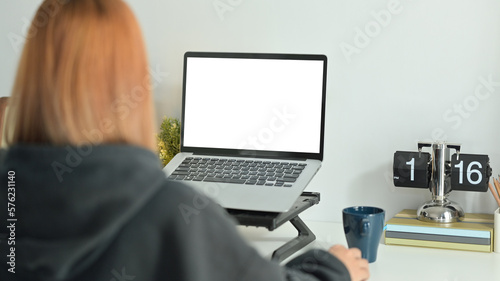 Back view of creative female freelancer sitting in comfortable workplace and working online with laptop computer