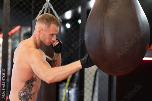 portrait of professional athlete muscular man boxer in red gloves in front of punching bag in fitness gym, in ring. © Елена Якимова