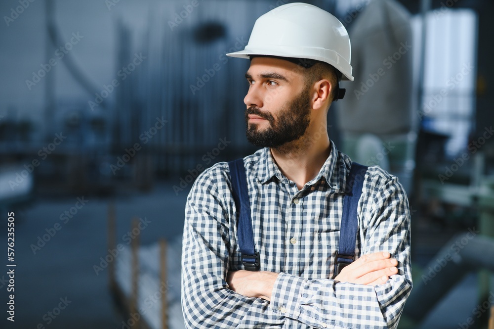 Portrait of Professional Heavy Industry Engineer Worker Wearing Safety Uniform, Hard Hat Smiling. In the Background Unfocused Large Industrial Factory. Portrait of Professional Heavy Industry Engineer Worker Wearing Safety Uniform, Hard Hat Smiling. In the Background Unfocused Large Industrial Factory.