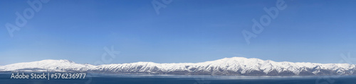 Aerial panorama view snow covered mountains. Snowy mountain ridge on winter sunrise. Stunning mountains range covered with snow over beautiful lake