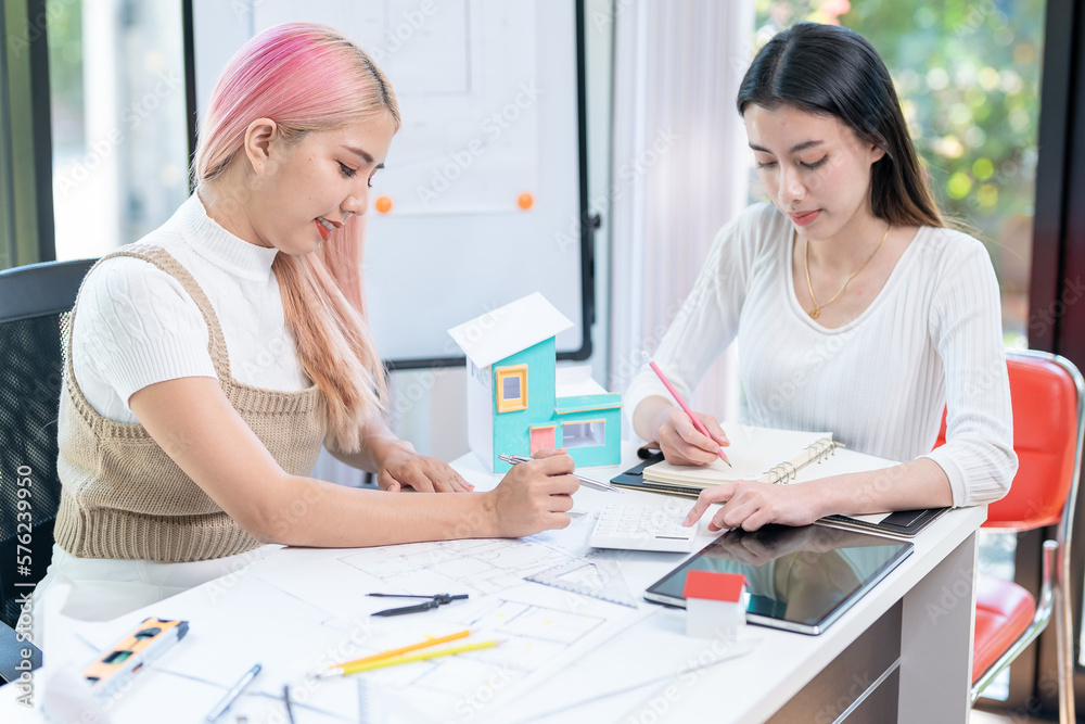 Concept of engineering consulting, Two female engineers discussing about model of building together; Two female architects are studying blueprint of building house. Concept of engineering consulting, Two female engineers discussing about model of building together; Two female architects are studying blueprint of building house.