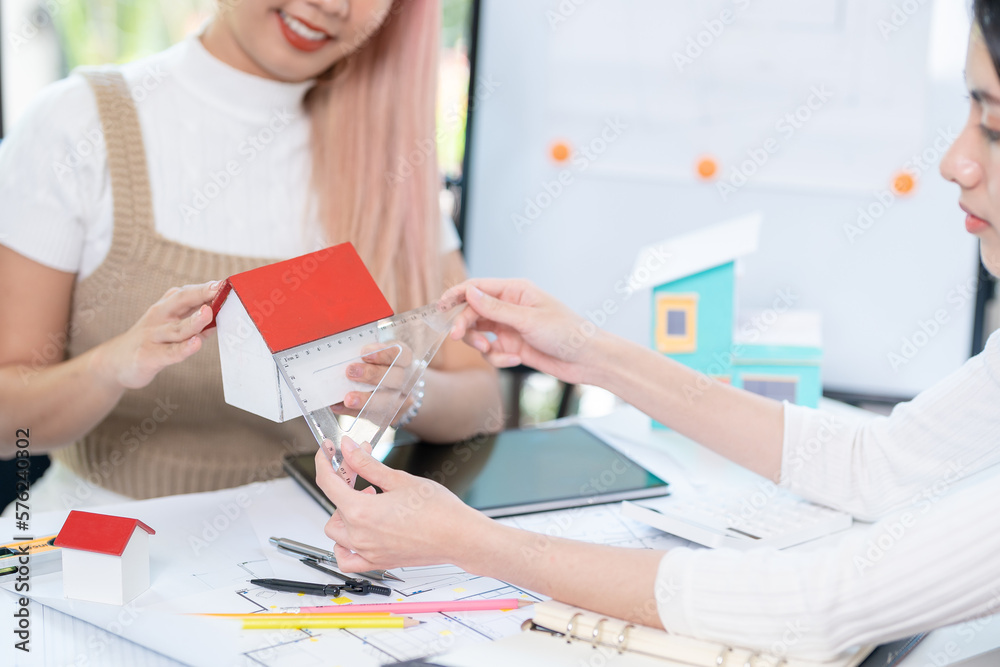 Concept of engineering consulting, Two female engineers discussing about model of building together; Two female architects are studying blueprint of building house. Concept of engineering consulting, Two female engineers discussing about model of building together; Two female architects are studying blueprint of building house.