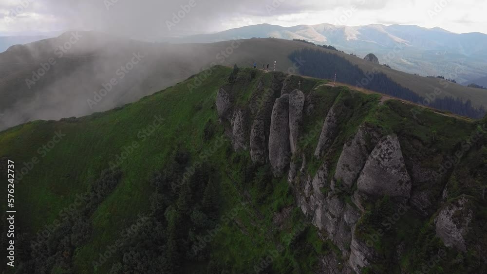 Aerial shot moving forward over a mountain ridge with clouds rolling in. he camera captures stunning views of the mountain peaks, valleys, and cliffs, highlighting their natural beauty and grandeur.