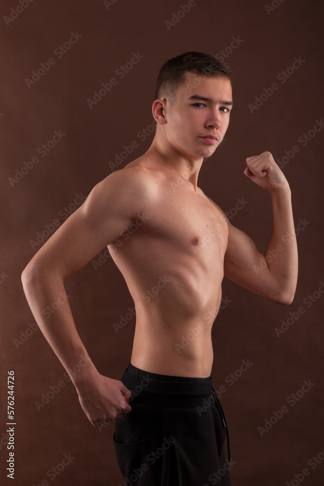 Handsome muscular shirtless adolescent boy flexing muscles.