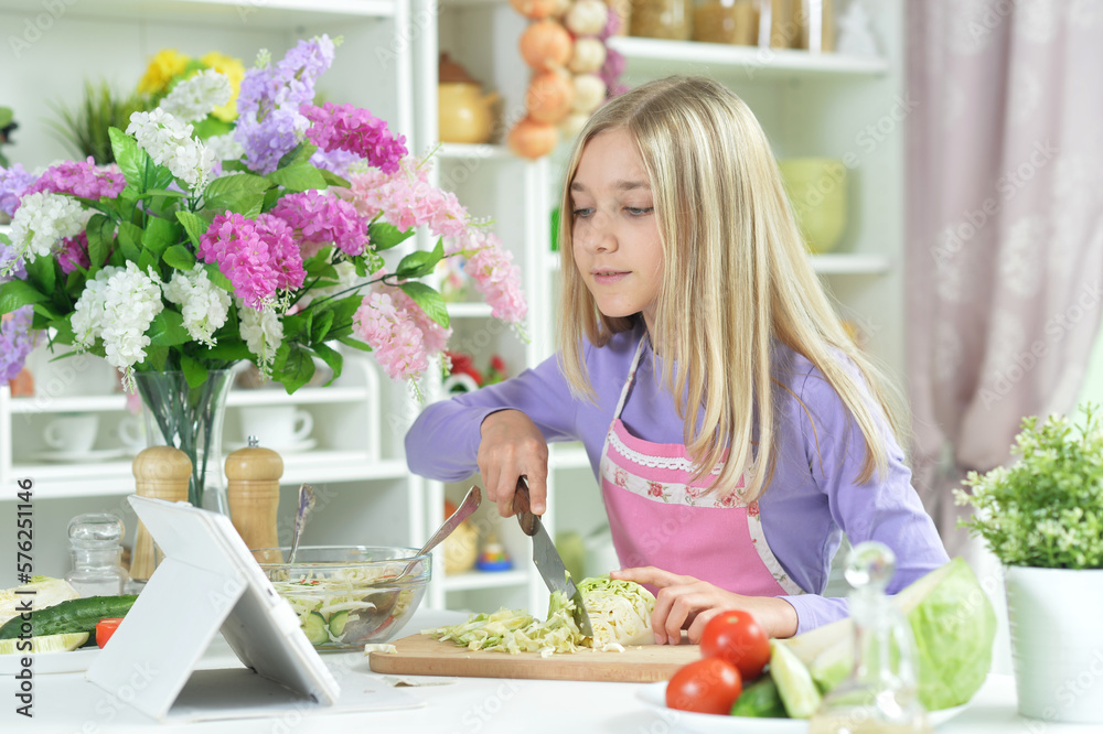 little girl cutting cabbage and looking at tablet at kitchen