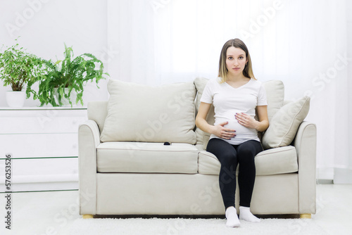 Pregnant woman sitting on white sofa and touching her stomach. Free Download Pregnant woman sitting on white sofa and touching her stomach. - GFXLoad
