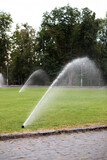 On green lawn, in a park or garden, a sprinkler is working. Automatic sprinkler irrigation system or device for watering of lawn. Grass irrigation. Garden Irrigation sprinkler watering lawn. Spraying	