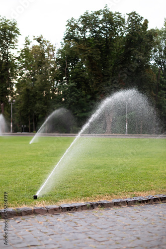 On green lawn, in a park or garden, a sprinkler is working. Automatic sprinkler irrigation system or device for watering of lawn. Grass irrigation. Garden Irrigation sprinkler watering lawn. Spraying 