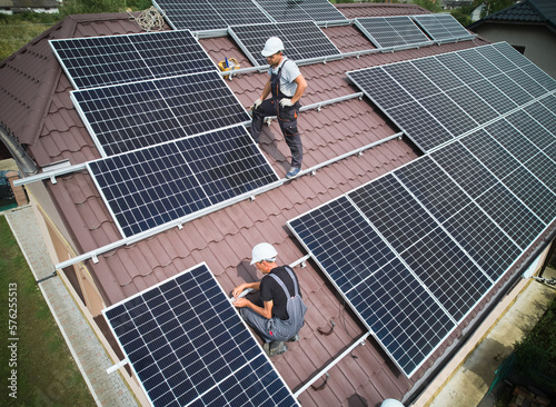 Men technicians building photovoltaic solar moduls on roof of house. Engineers in helmet installing solar panel system outdoors. Concept of alternative and renewable energy. Aerial view.