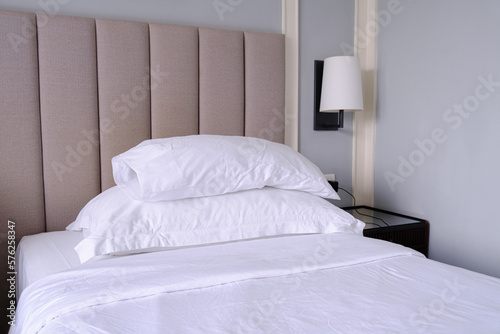 Clean white bed in the bedroom. Bed with white linens, bedside table and wall sconce. Hotel room after cleaning.