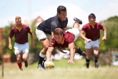 This game is not for the faint hearted. Full length shot of a young rugby player scoring a try mid tackle. © Cameron M/peopleimages.com