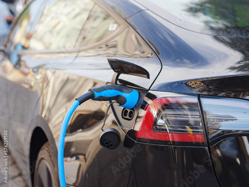 Munich, Germany - August 5, 2022 : Electric car with opened charging socket cap and charger plugged in, at a public electric charging station in city