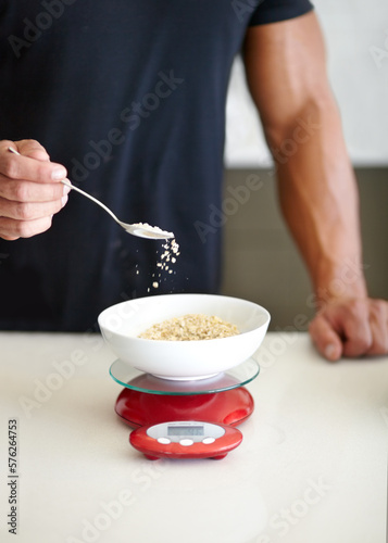 Portioning is key. Cropped view of a muscular man measuring his oats on a scale for breakfast.