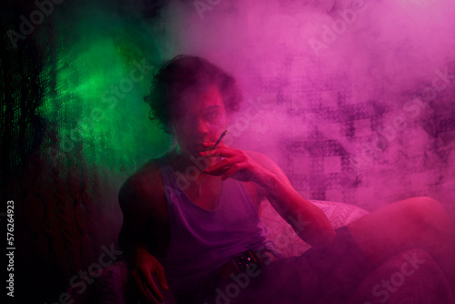 Intoxicated guy smoking cigarette in armchair in colorful smoke