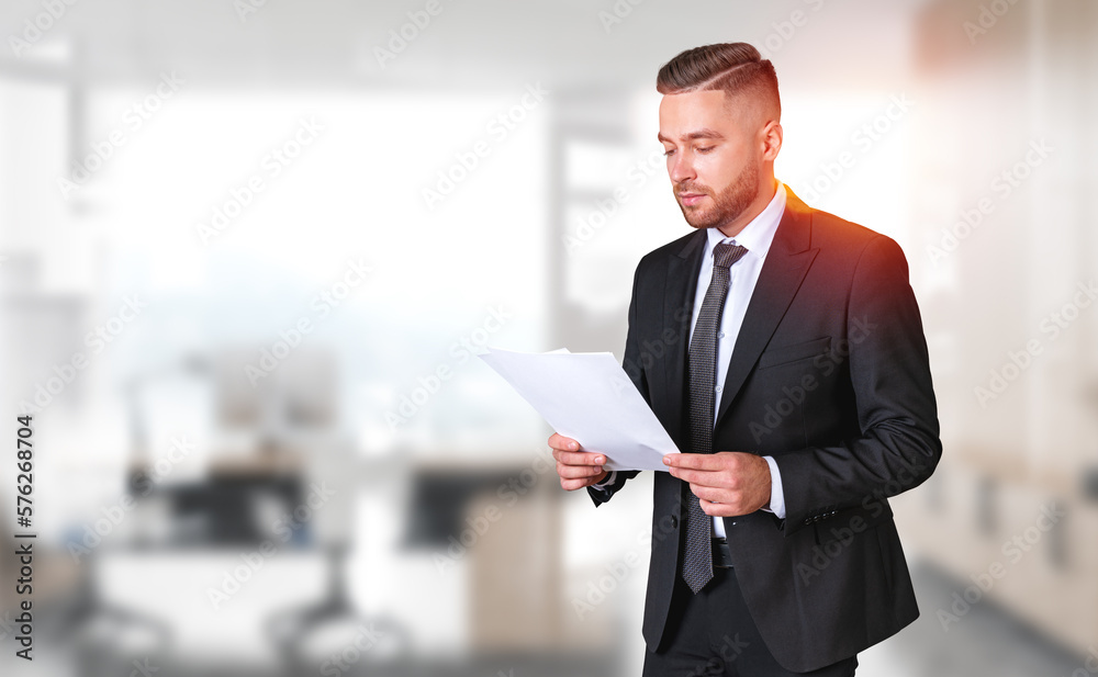 Bearded young businessman in blurry office with documents