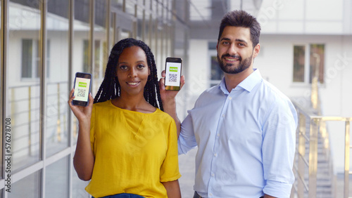 Foto Multiethnic couple looking at camera showing vaccinated qr-code on cellphone