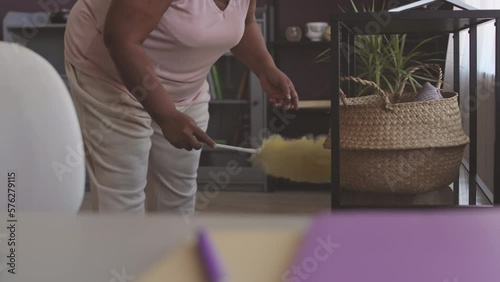Cropped shot of unrecognizable Black woman using feather duster while cleaning living room