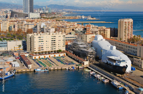 Shipbuilding. Unfinished large ships during construction surrounded by scaffold on dry dock  in shipyard at the port of Barcelona. Large colorful fishing nets on the ground. Barcelona, Spain