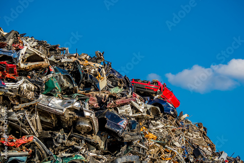 Front view of a red car atop a pile of compressed and crumpled car wrecks in a junkyard, conveying the urgent need for car recycling and waste management in the automobile industry, copy space on top.