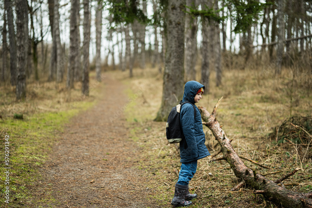 Boy with backpack and rain boots in the forest.