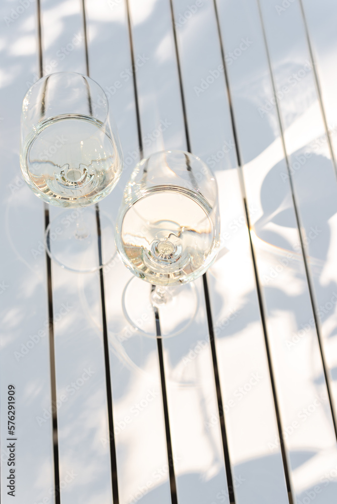 Two glasses of white wine on a white table outdoors.