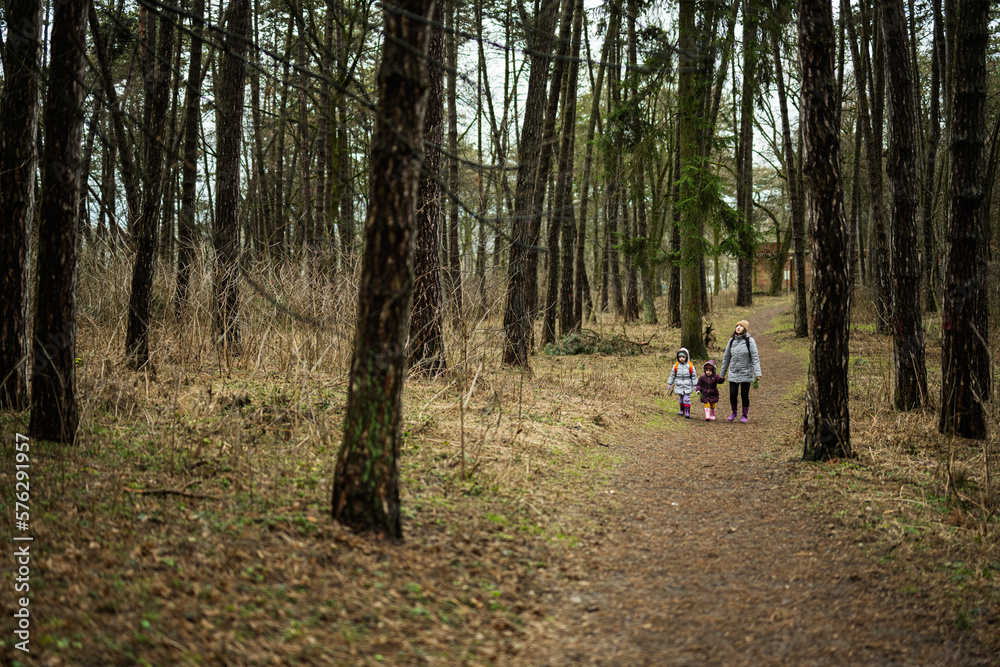 Mother and two daughters with backpacks walking along the forest road together. Mother and two daughters with backpacks walking along the forest road together.