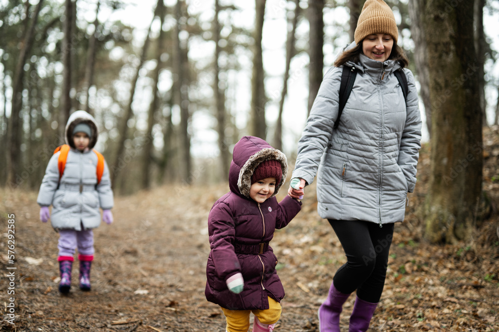 Mother and two daughters with backpacks walking along the forest road together. Mother and two daughters with backpacks walking along the forest road together.