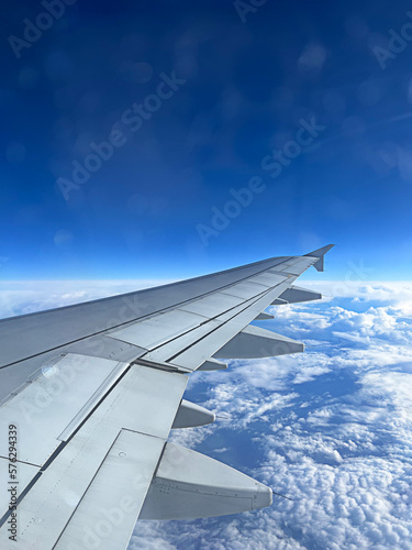 view of the wing of a plane hovering over dense clouds in the blue sky, the concept of travel and freedom