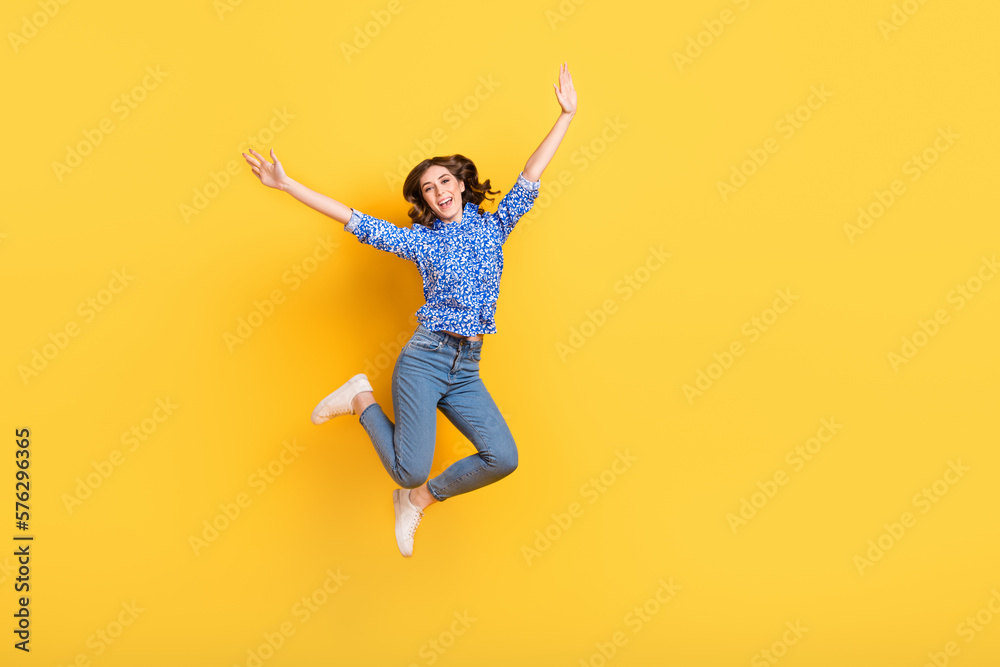 Full size photo of cheerful overjoyed girl jumping raise hands empty space isolated on yellow color background