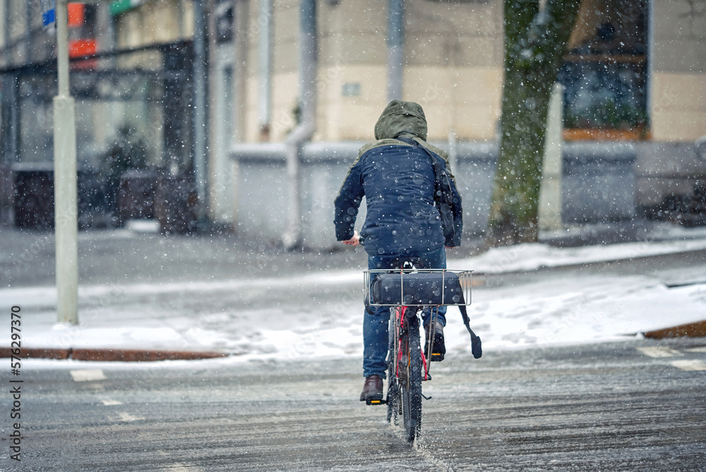 Man deliver pizza on bicycle cycling on snowy street in winter season. Delivery food service, delivery courier on bike. Delivery boy with pizza, restaurants delivery service cycling on snowy road