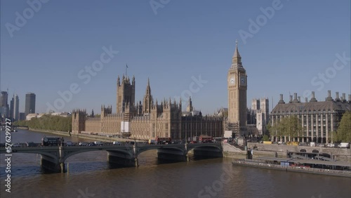Aerial drone shot flying towards Westminster Bridge, Westminster Abbey and Big Ben over the River Thames with London Buses and traffic crossing Westminster Bridge on a bright clear sunny day.
