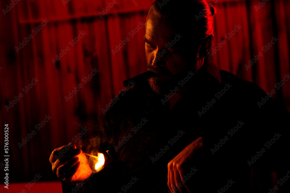 Man with cigar in mouth looking thoughtfully at lit match at night