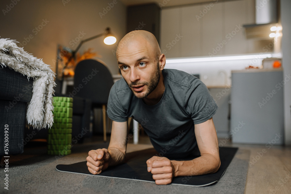 A bearded man is doing sports in his apartment standing plank