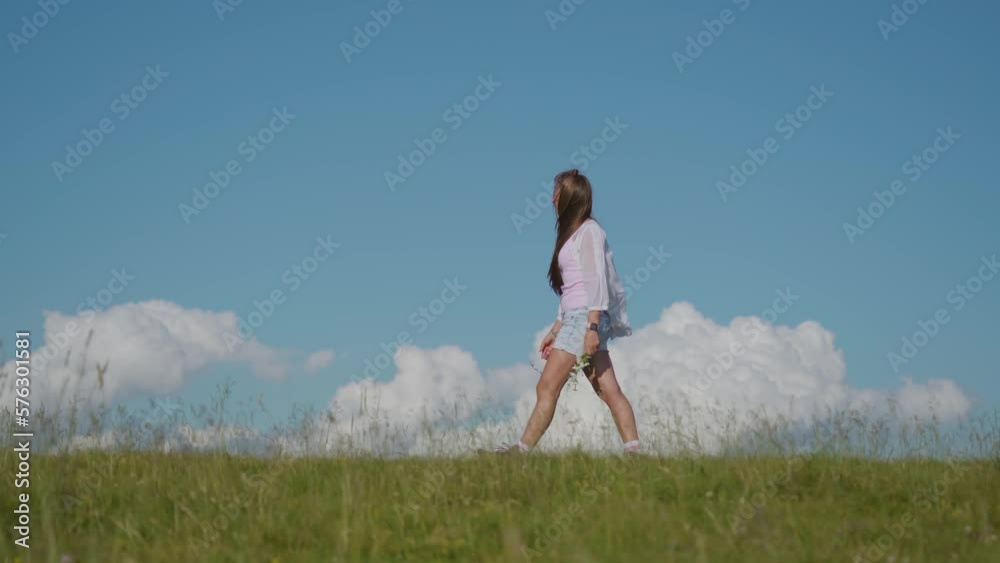 Girl walks on the green grass with blue sky in the background