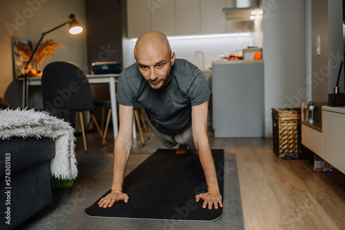 A motivated man in sportswear is busy with training standing on his arms on a stylish carpet in a modern apartment in his spare time.