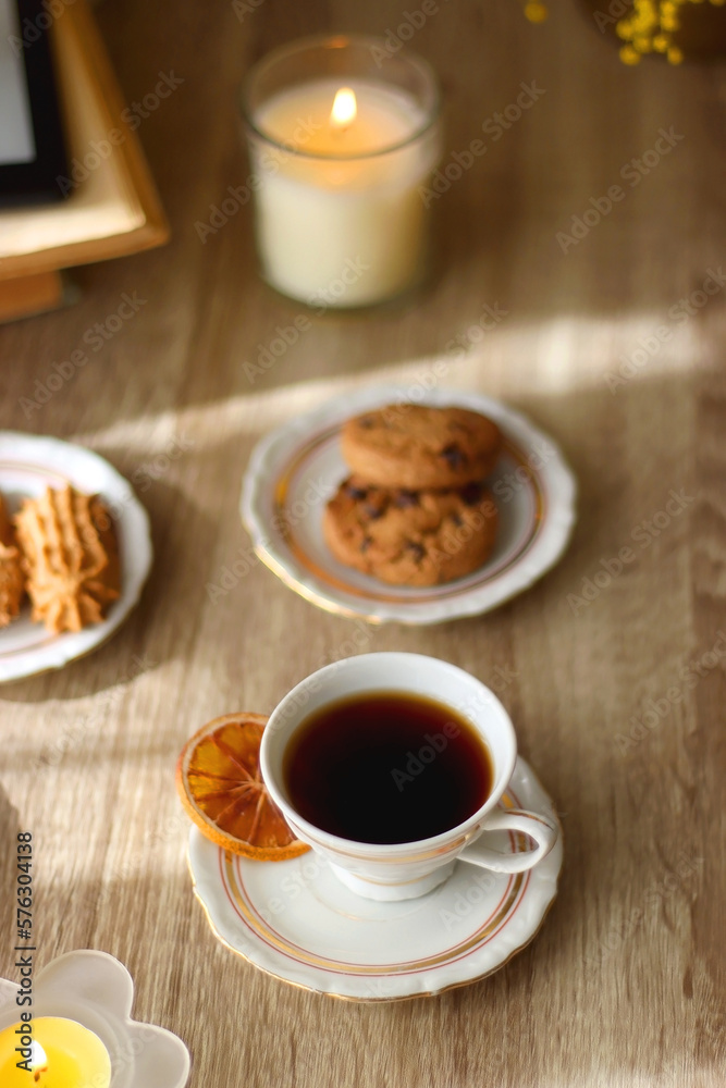 Scented candles, chocolate, cookies, cup of tea, books, e-reader, glasses and flowers on the table. Hygge at home. Selective focus.